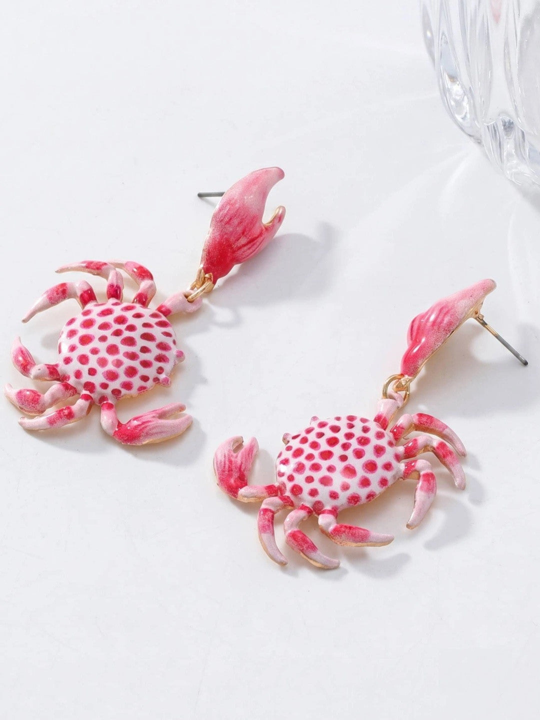 Two pink enamel crab drop earrings with white polka-dot shell body and gold-tone claw studs on white surface