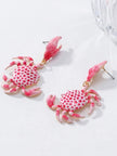 Two pink enamel crab drop earrings with white polka-dot shell body and gold-tone claw studs on white surface