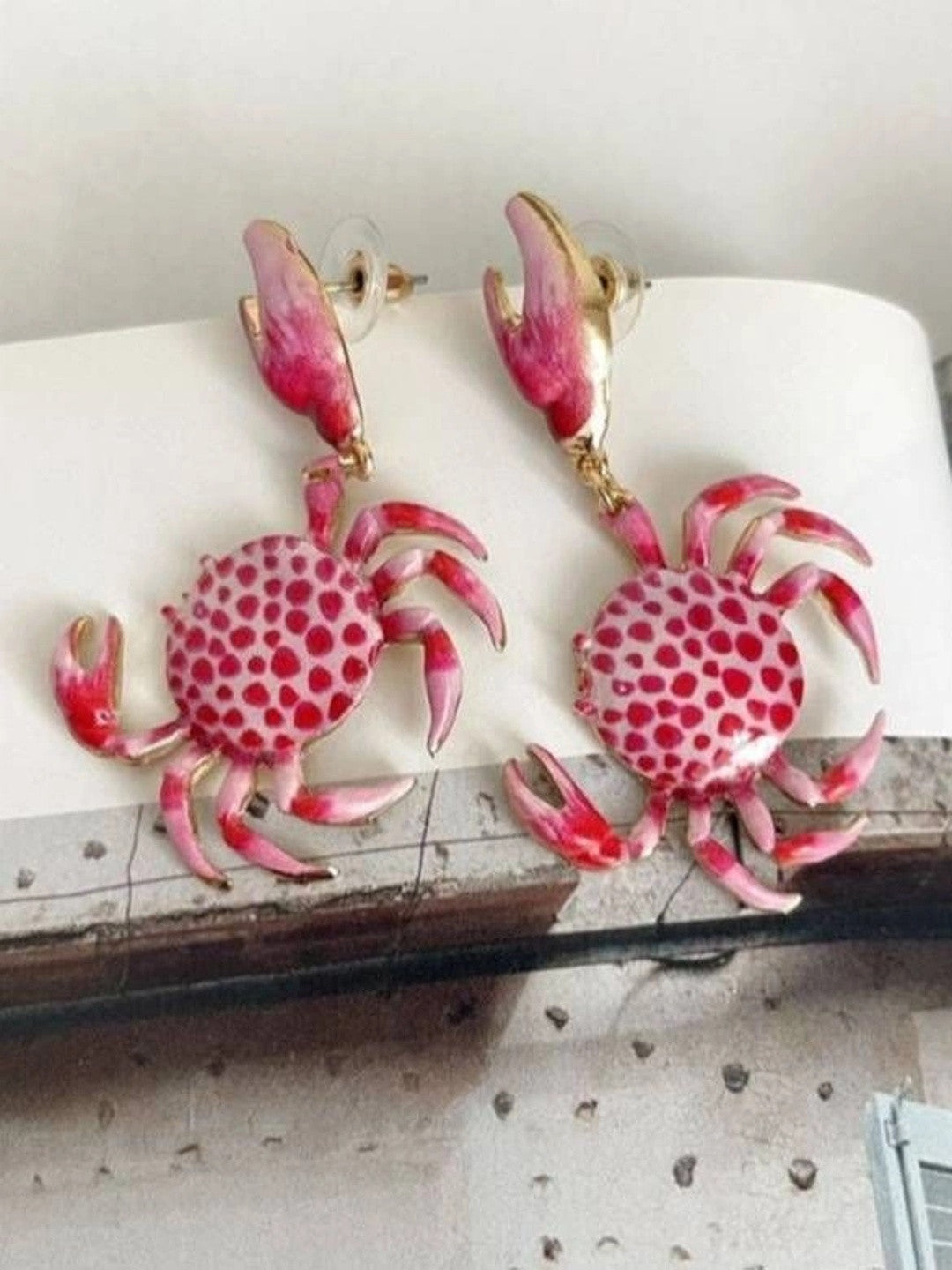 Pair of pink crab drop earrings with push-back closures resting on open pages of a book