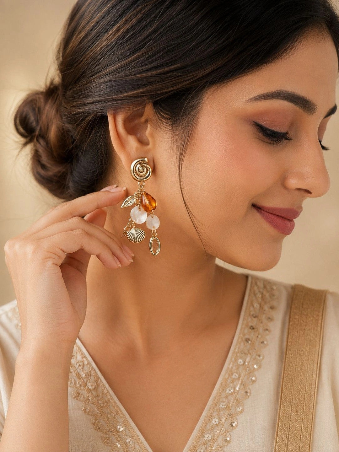 Woman wearing gold shell charm drop earrings with amber bead and spiral stud post on her ear