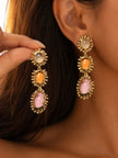 Model holding one gold-plated triple drop earring while wearing the other, displaying full length of both earrings
