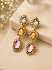 Pair of gold-plated triple drop earrings laid flat on cream surface with dried floral backdrop