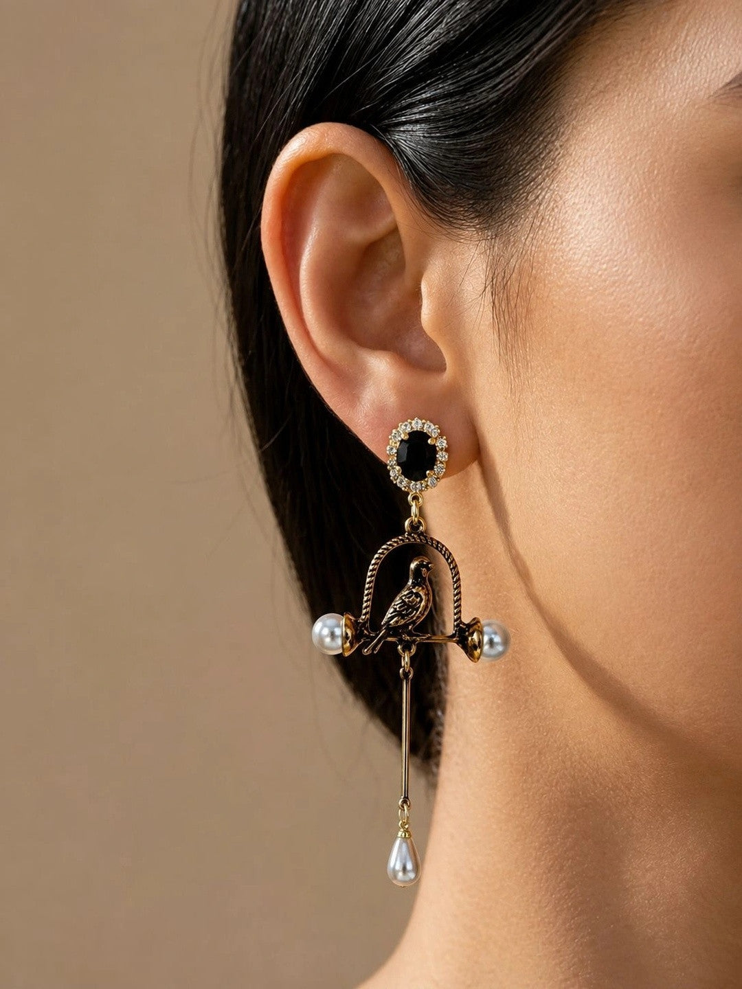 Antique gold bird cage drop earring worn on a woman's ear, showing parrot figurine, pearl accents, and black crystal stud