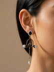 Antique gold bird cage drop earring worn on a woman's ear, showing parrot figurine, pearl accents, and black crystal stud