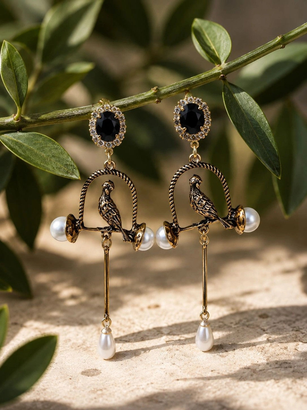 Pair of bird cage drop earrings hanging from a branch, showing twisted arch, parrot perch, and pearl teardrop dangles