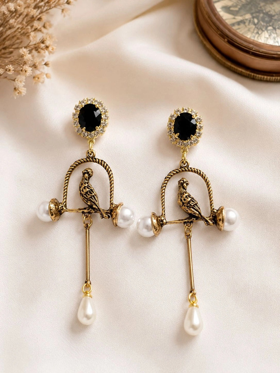 Both bird cage earrings laid flat on ivory silk fabric, showing black crystal halo studs and full drop length