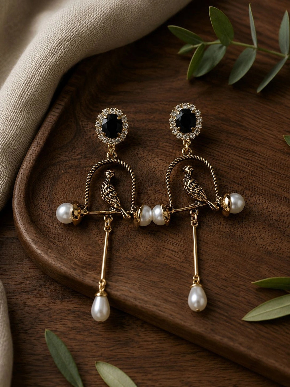 Pair of antique gold parrot cage earrings displayed on a dark wooden tray with eucalyptus leaves