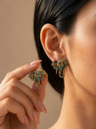 Woman wearing antique gold elephant head stud earrings with turquoise stones, holding second earring between fingers