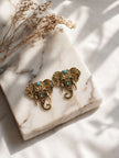 Two antique gold elephant stud earrings placed on white marble surface with dried floral stems in background