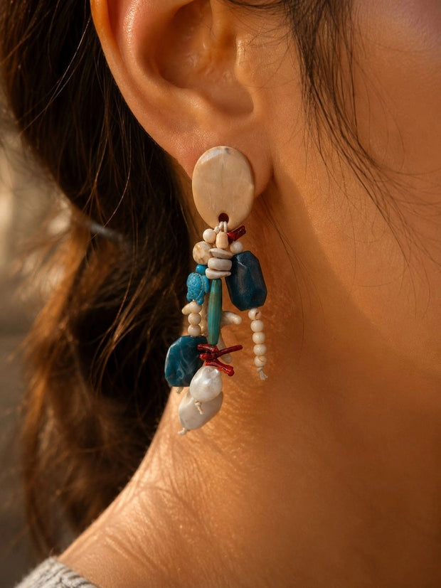 Woman wearing ocean-theme beaded drop earring with teal stones, red coral beads and faux pearl drop