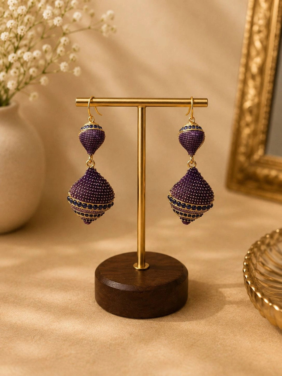 Pair of purple CZ geometric drop earrings hanging on a gold brass jewellery stand with wooden base