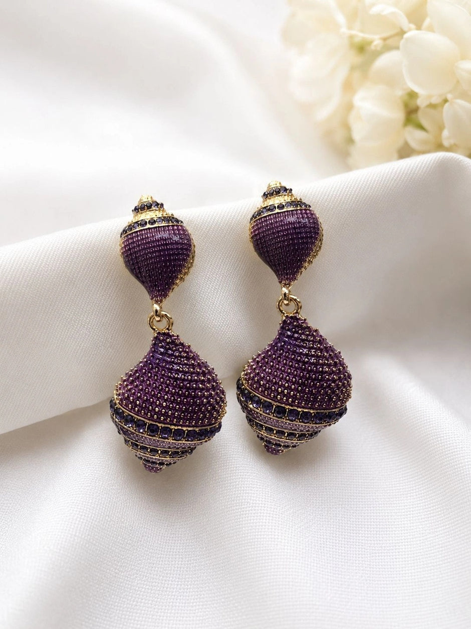 Close-up of two purple cubic zirconia two-tier drop earrings laid flat on white satin fabric