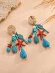 Pair of turquoise beaded starfish drop earrings laid flat on a cream surface with coral and shell accents