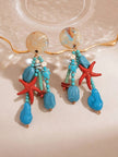 Close-up of both earrings showing shell-finish resin studs, sea turtle charm, and layered turquoise bead strands