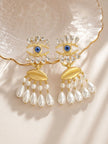 Both gold evil eye earrings displayed flat on a pearlescent shell dish in warm light