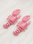 Two pink lobster earrings placed side by side on a white marble surface