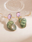 Pair of green shell and pink crystal drop earrings resting on a rippled glass tray, showing the open shell aperture with pale blue interior