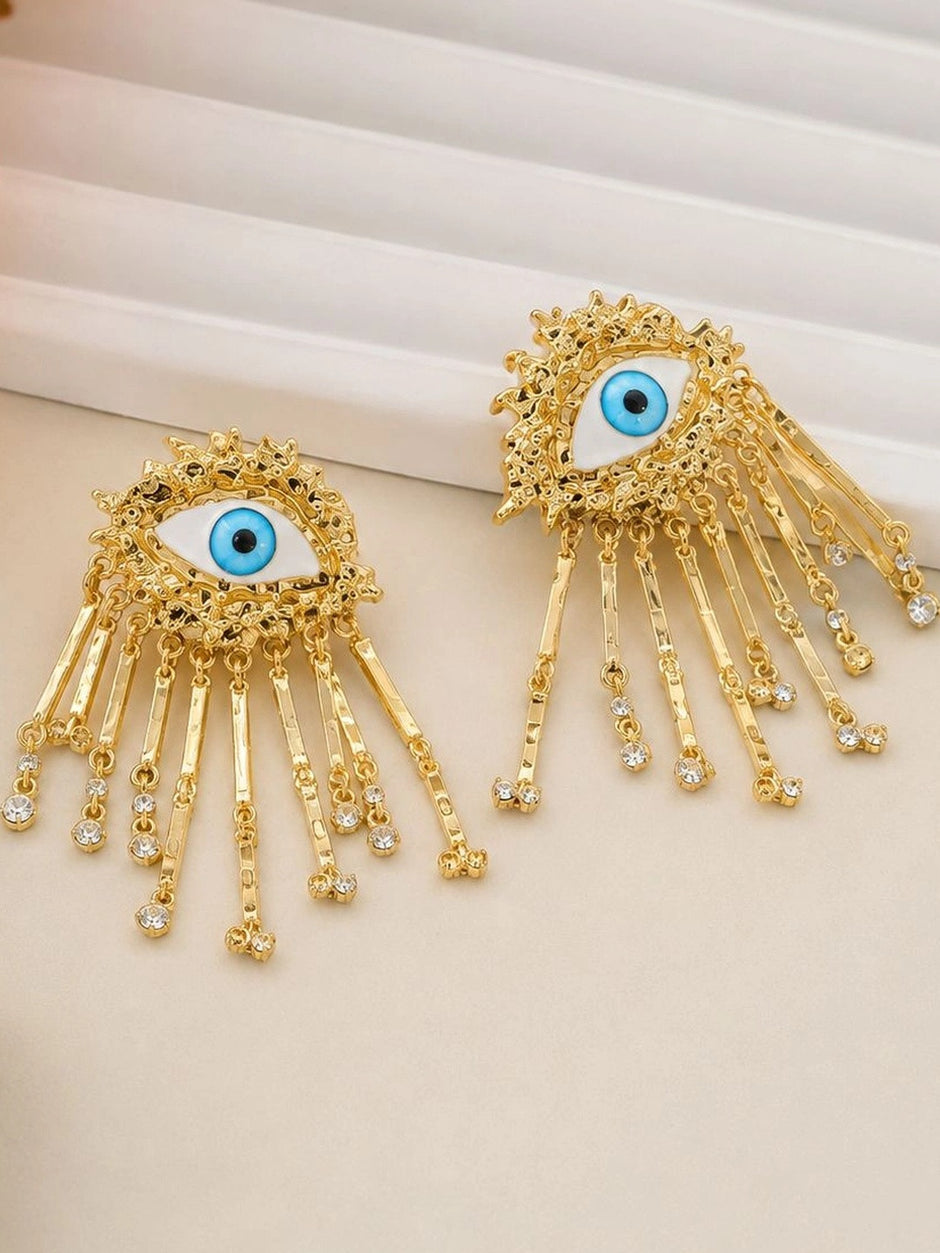 Close-up of gold evil eye tassel earrings showing rhinestone-tipped bar dangles and sunburst frame detail