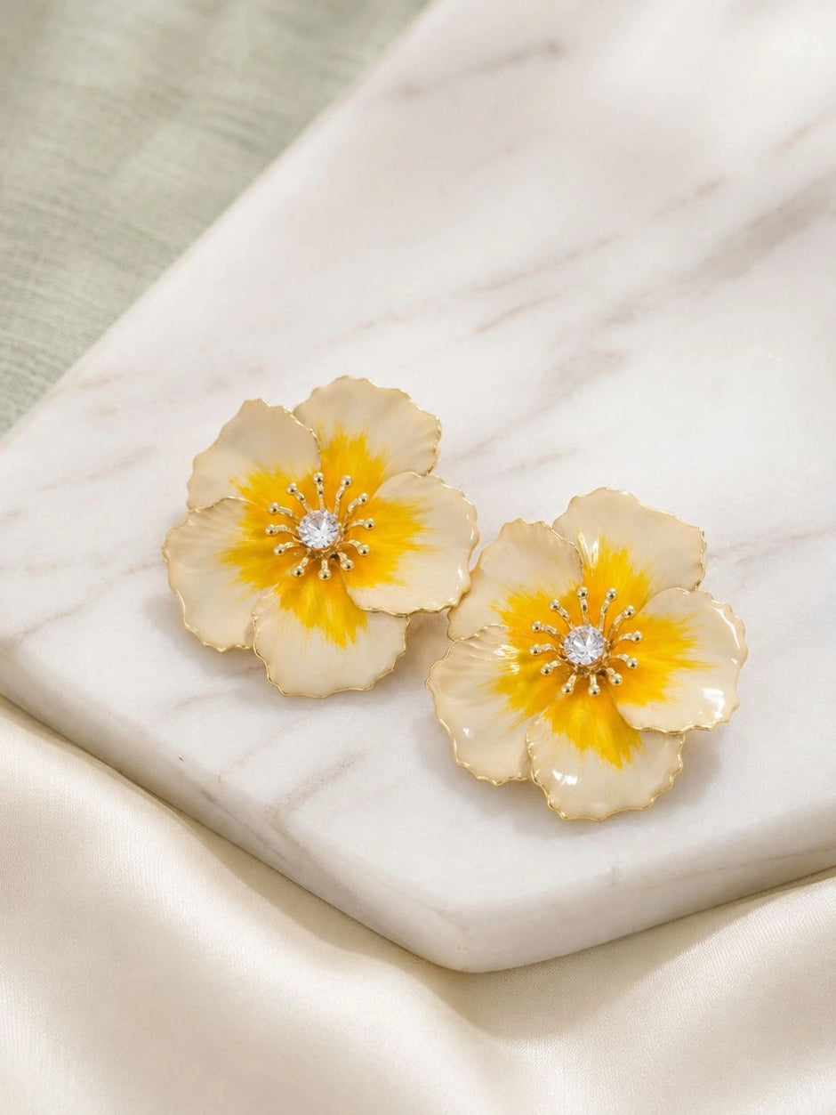 Pair of ivory and yellow enamel flower stud earrings with crystal centres on a marble surface