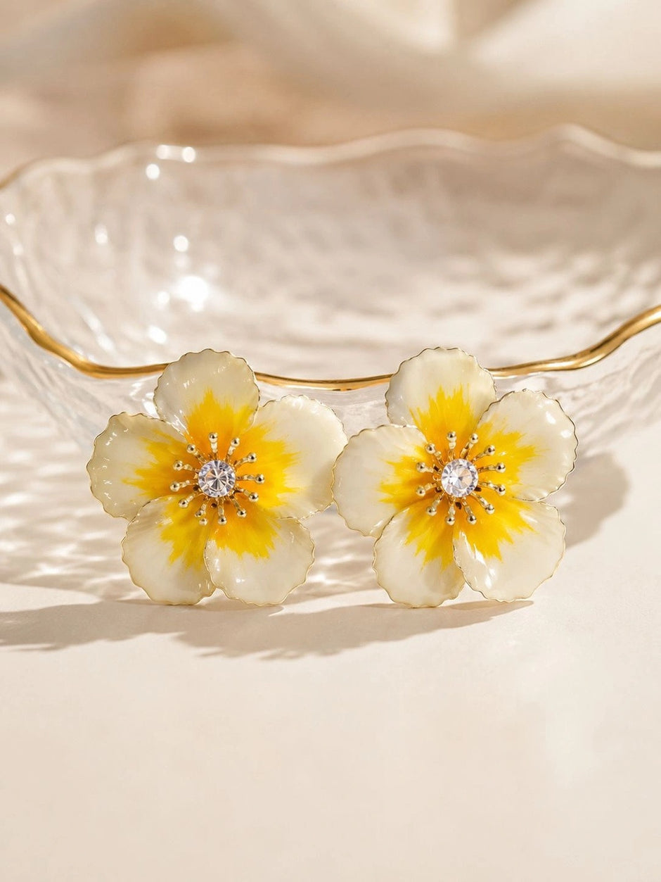 Ivory and yellow enamel flower stud earrings resting against edge of gold-rimmed glass dish