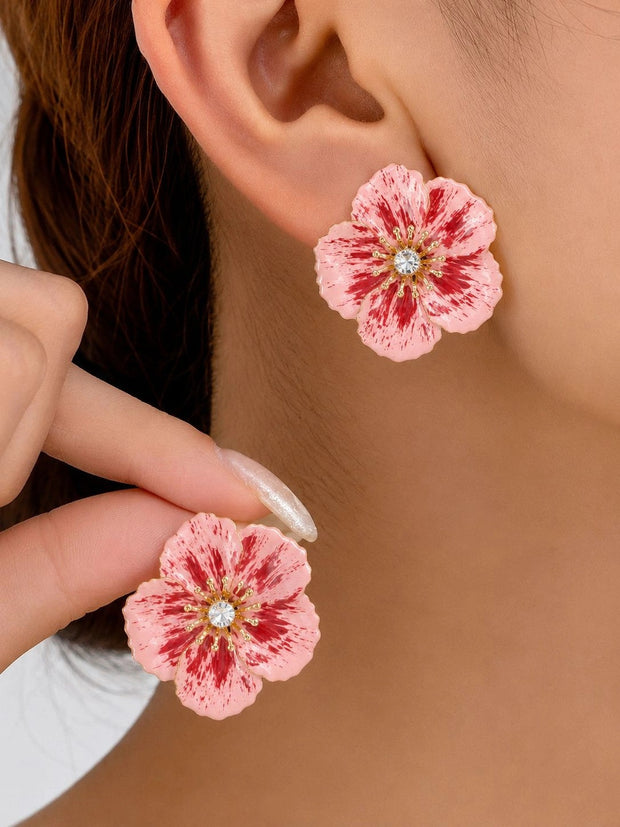 Pink enamel flower stud earring worn on ear with second earring held between fingers