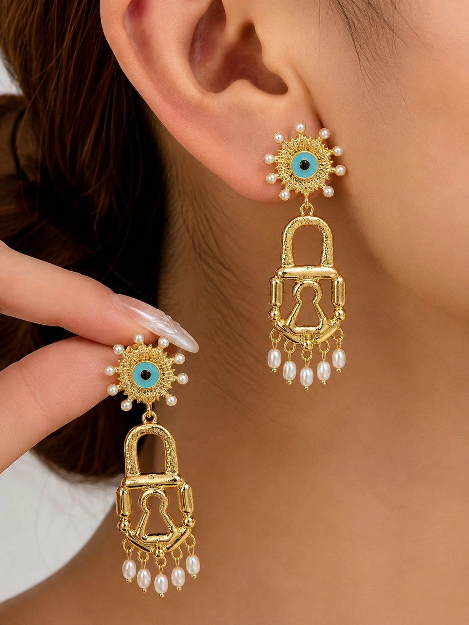 Close-up of gold evil eye lock earring being held near an ear showing keyhole cutout detail