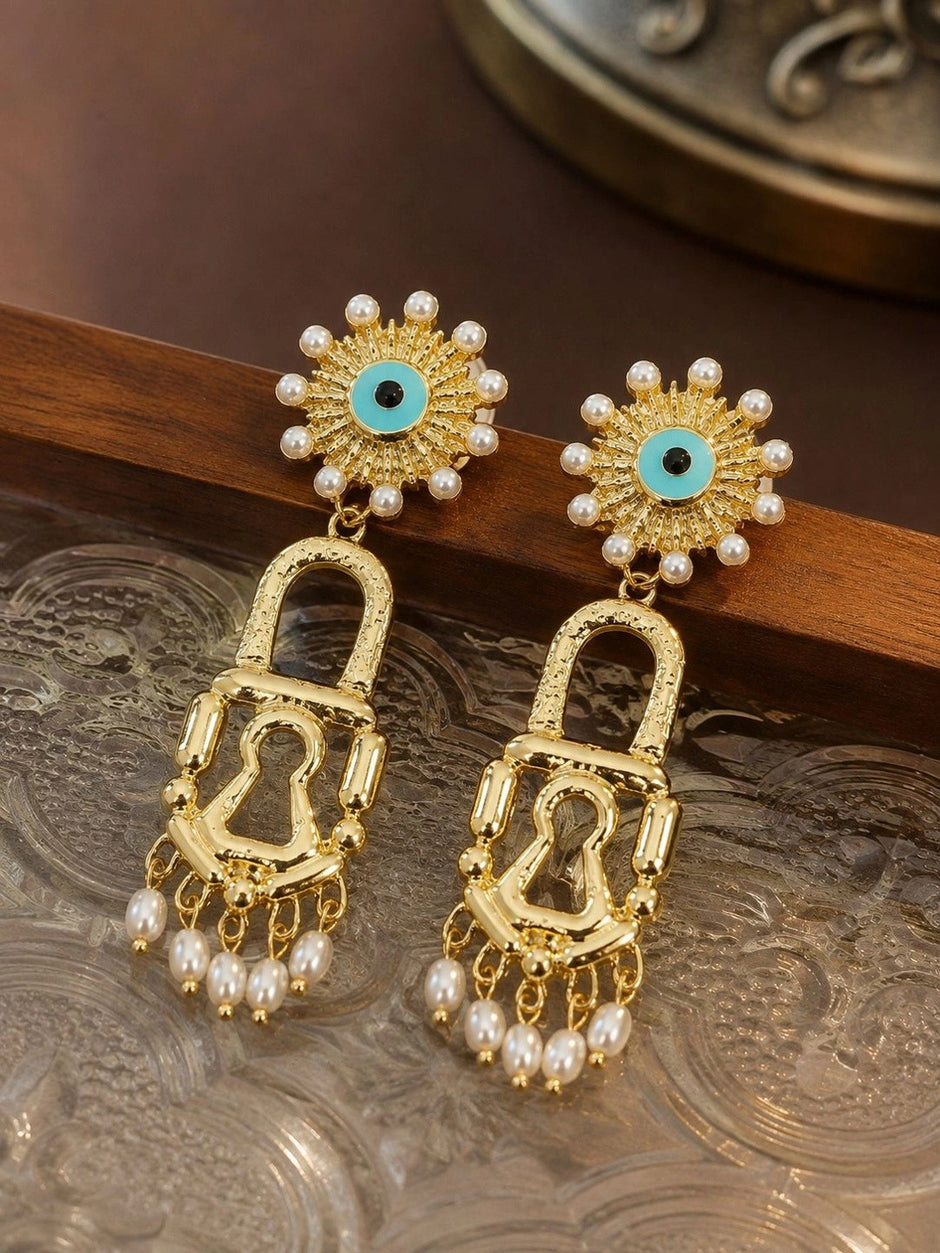 Gold padlock drop earrings with turquoise evil eye tops resting on a wooden surface