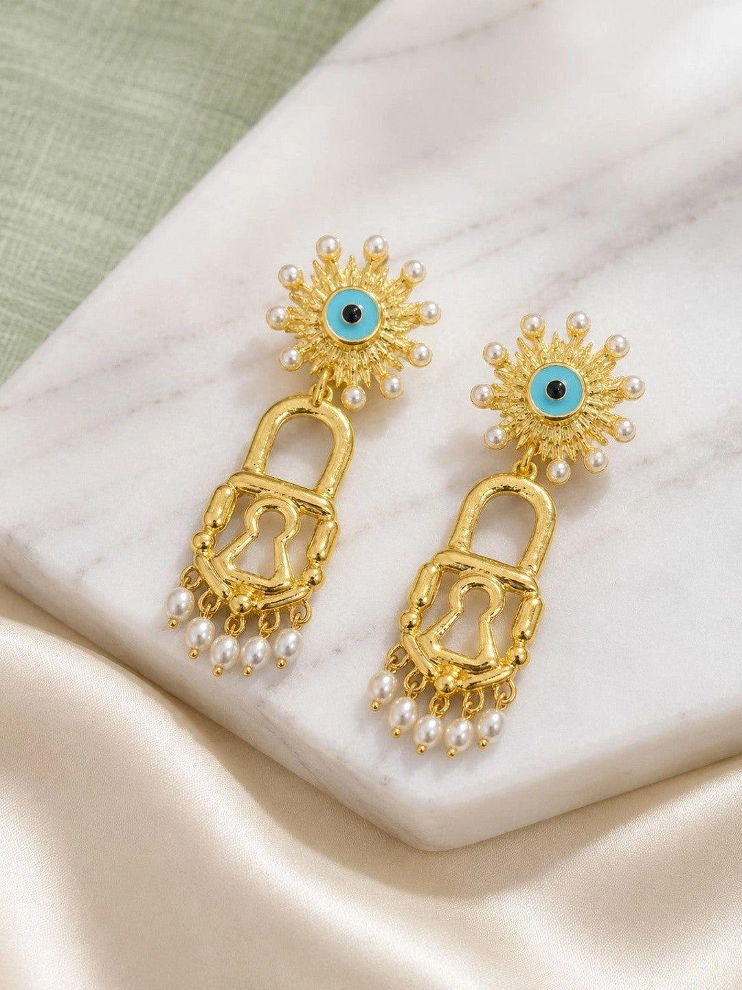 Gold evil eye lock earrings with pearl fringe displayed on a white marble surface