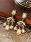 Close-up of gold evil eye pearl drop earrings resting on a carved metal tray showing textured detailing