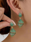 Woman holding and wearing green pavé crystal shell drop earrings against her ear, close-up side view