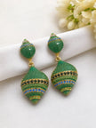 Two green crystal shell drop earrings with blue and black stone bands resting on white fabric near white flowers