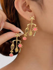 Close-up of gold tropical charm drop earring worn on a woman's ear, showing starfish stud and dangling charms