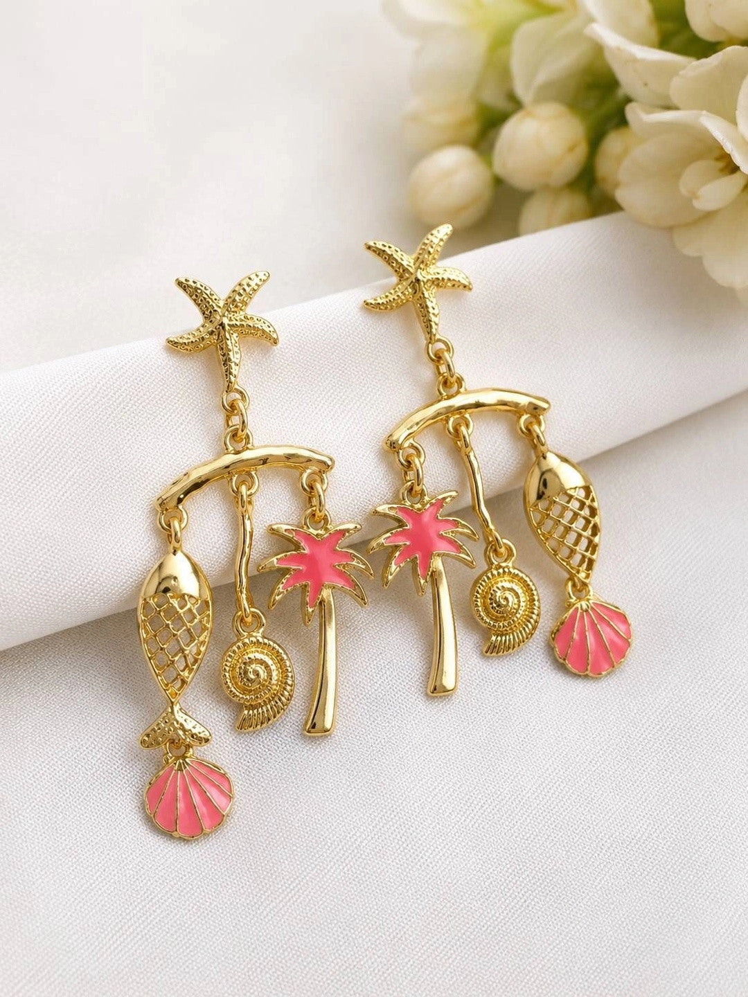Pair of gold-plated tropical earrings with pink enamel palm tree and scallop shell charms on white fabric