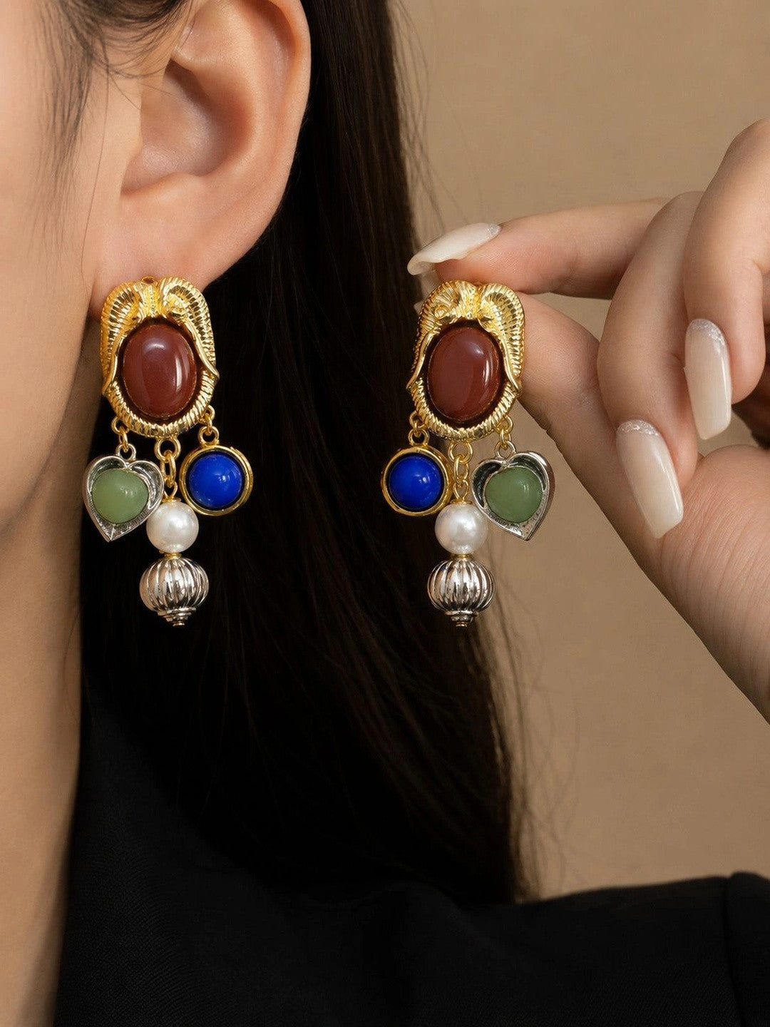 Gold-tone charm drop earrings with red cabochon stud worn on a woman's ear, showing cobalt blue, sage green and pearl charms