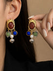 Gold-tone charm drop earrings with red cabochon stud worn on a woman's ear, showing cobalt blue, sage green and pearl charms
