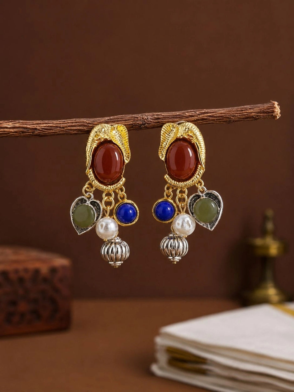 Pair of multi-stone charm drop earrings hanging from a wooden branch against a warm brown background