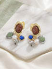 Pair of gold and silver-tone multi-charm drop earrings displayed on a white marble surface with green fabric backdrop
