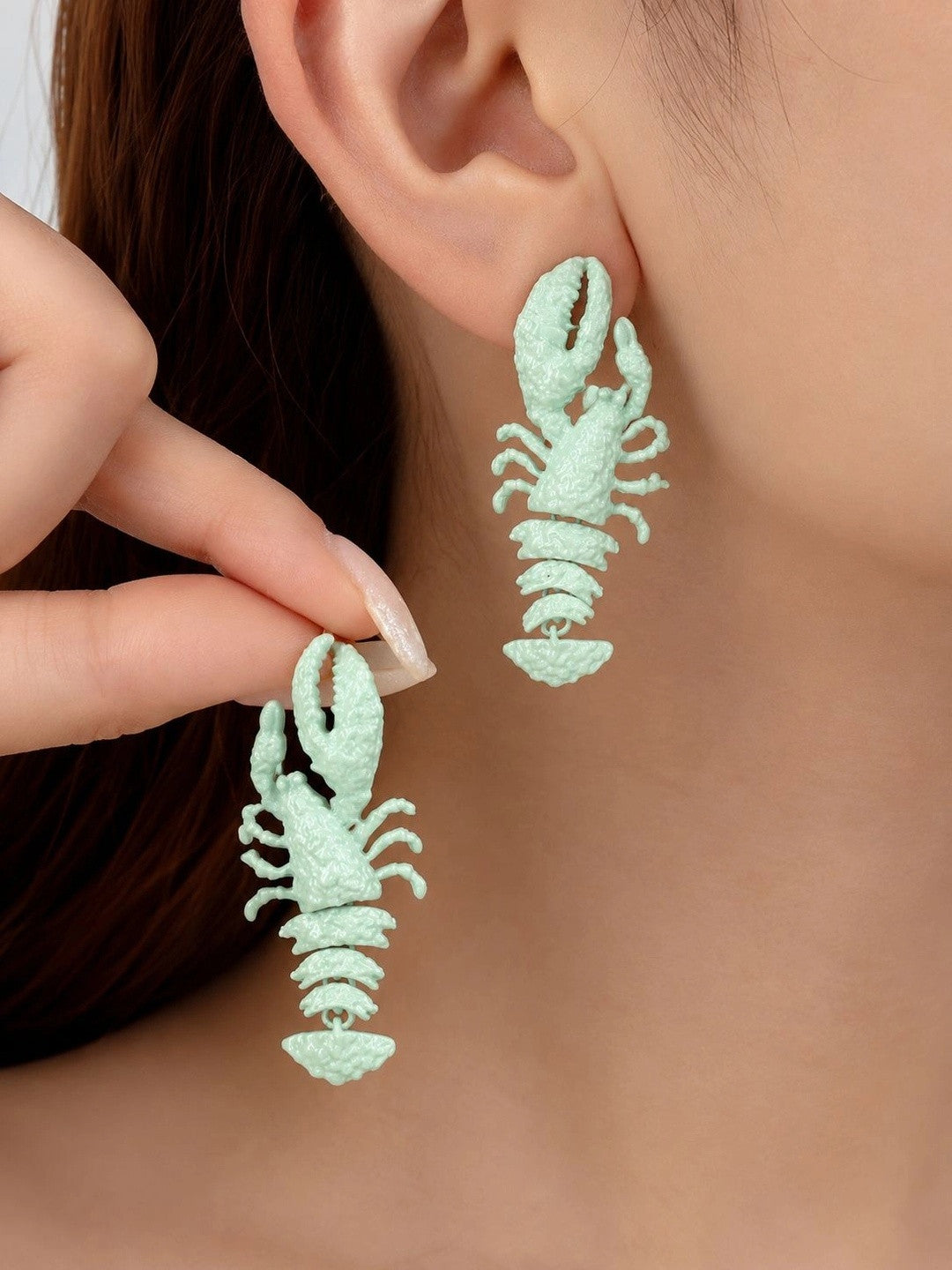 Model wearing and holding mint green lobster drop earrings close to her ear