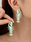 Model wearing and holding mint green lobster drop earrings close to her ear