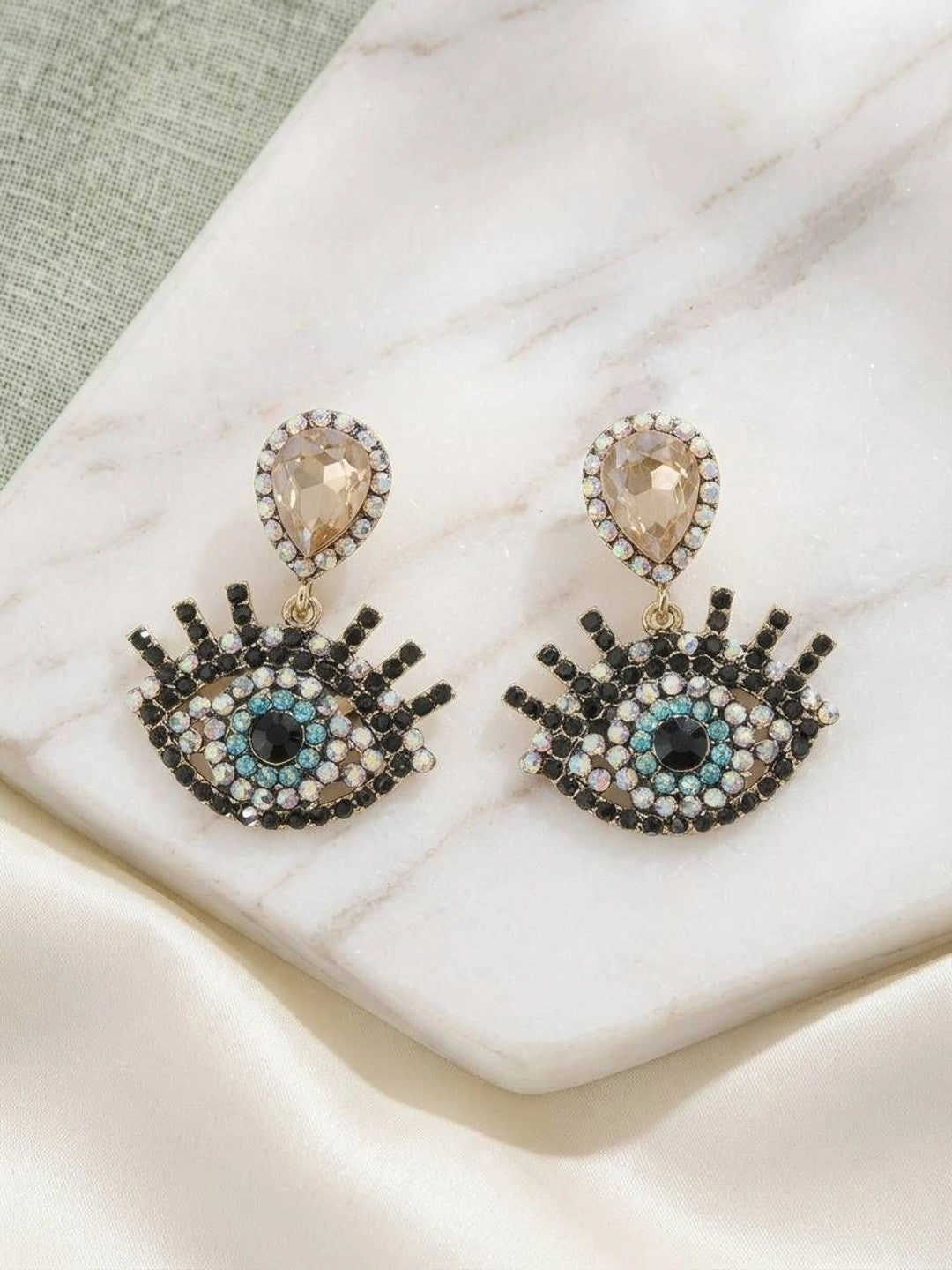 Pair of evil eye drop earrings on marble surface showing full front view of rhinestone detailing