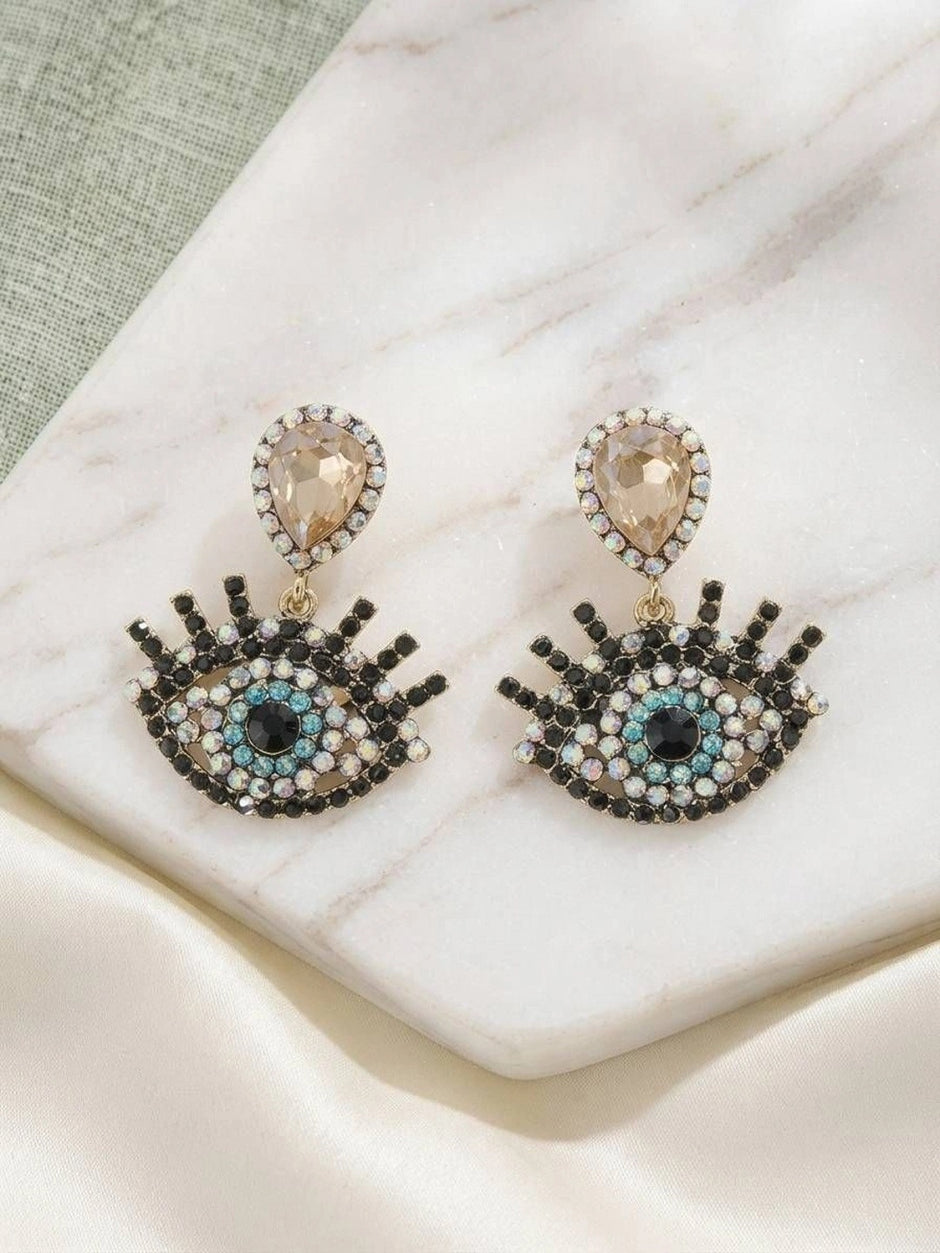 Pair of evil eye drop earrings on marble surface showing full front view of rhinestone detailing