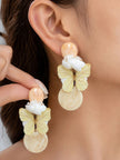 Close-up of resin butterfly drop earrings worn on a model's ear, showing yellow butterfly and white flower over cream marbled disc