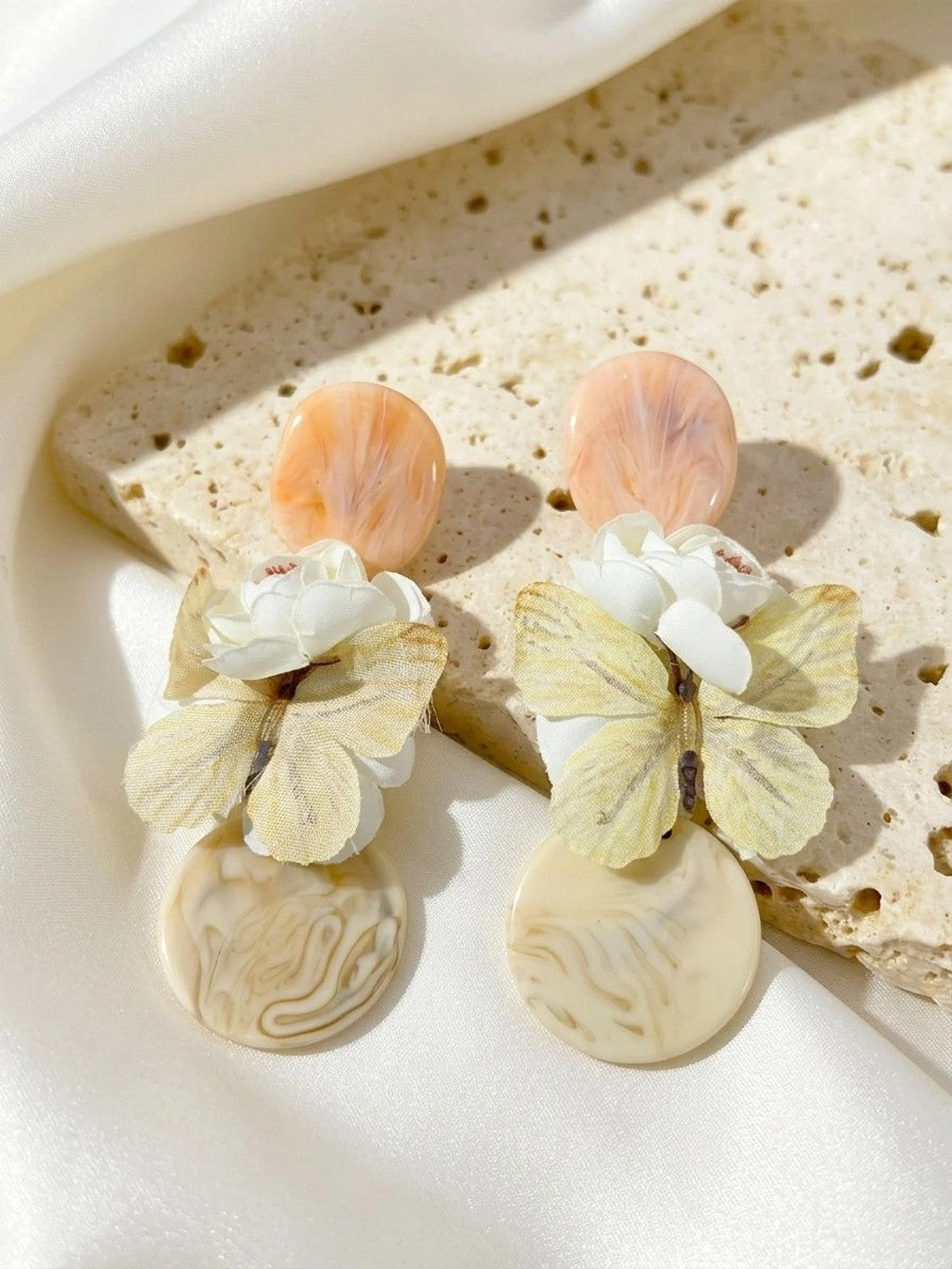 Both resin butterfly drop earrings laid on a textured stone surface in natural light, showing butterfly and floral detail clearly