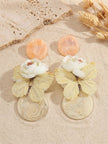 Peach and cream resin butterfly drop earring pair displayed on sand with dried wheat stalks in warm sunlight