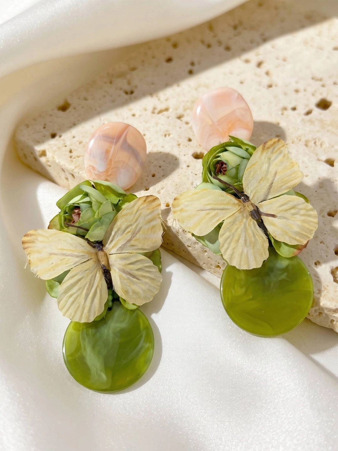 Two butterfly floral drop earrings resting on a textured stone surface in natural light