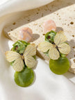 Two butterfly floral drop earrings resting on a textured stone surface in natural light