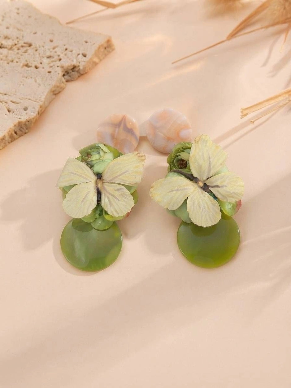 Green resin butterfly earrings with marbled peach studs displayed on a soft pink surface