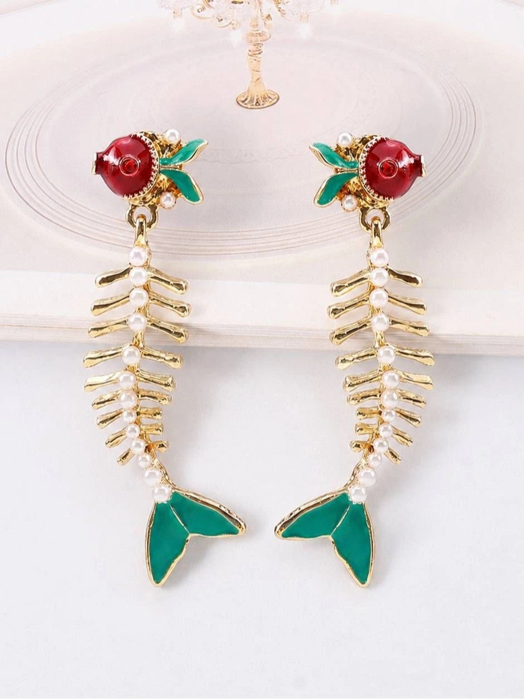 Pair of gold fish skeleton earrings with faux pearl spine laid flat on white surface