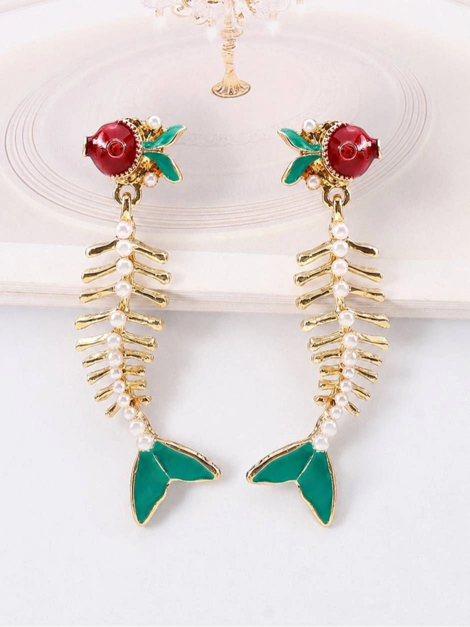 Pair of gold fish skeleton earrings with faux pearl spine laid flat on white surface