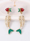 Pair of gold fish skeleton earrings with faux pearl spine laid flat on white surface